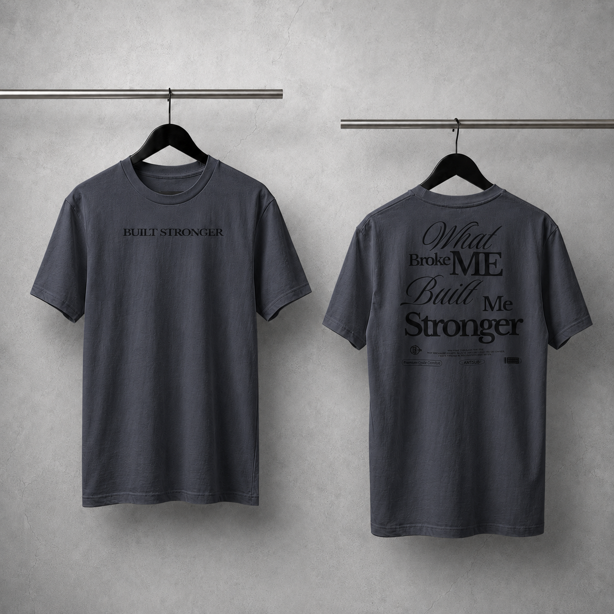 Two gray t-shirts with motivational text on hangers against a gray wall.